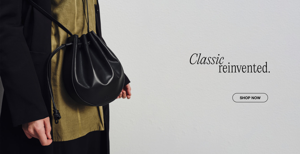 Person holding a black handbag with 'Classic reinvented' text and 'Shop Now' button on a light gray background.